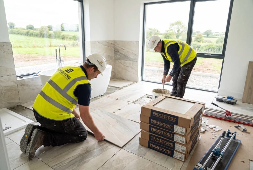 Primestone installers laying light marble-effect tiles in a bright bathroom with freestanding bath